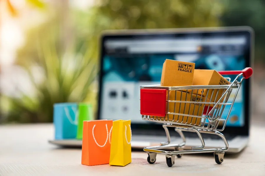 Carrinho de compras em miniatura e sacolas diante de um notebook